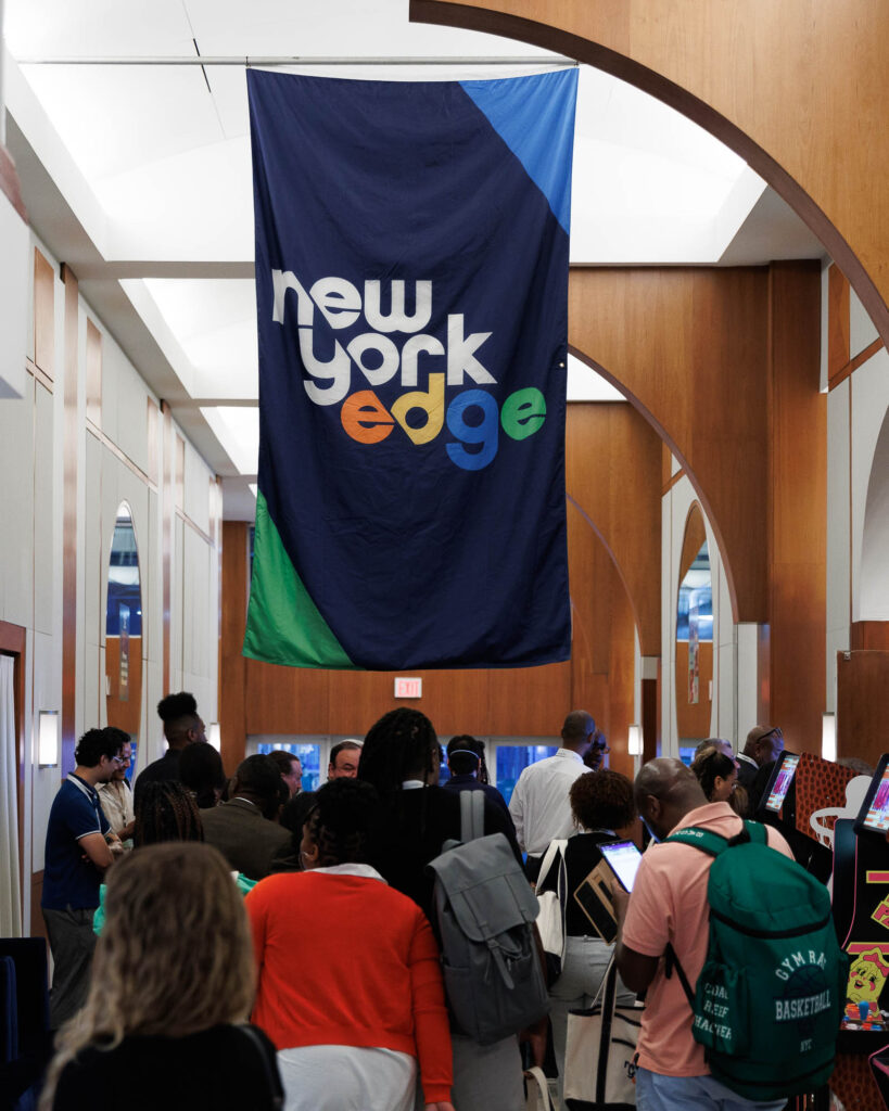 Attendants to the New York Edge's Power of Us Conference gathering at entrance hall. A banner with the New York Edge's logo flying above them